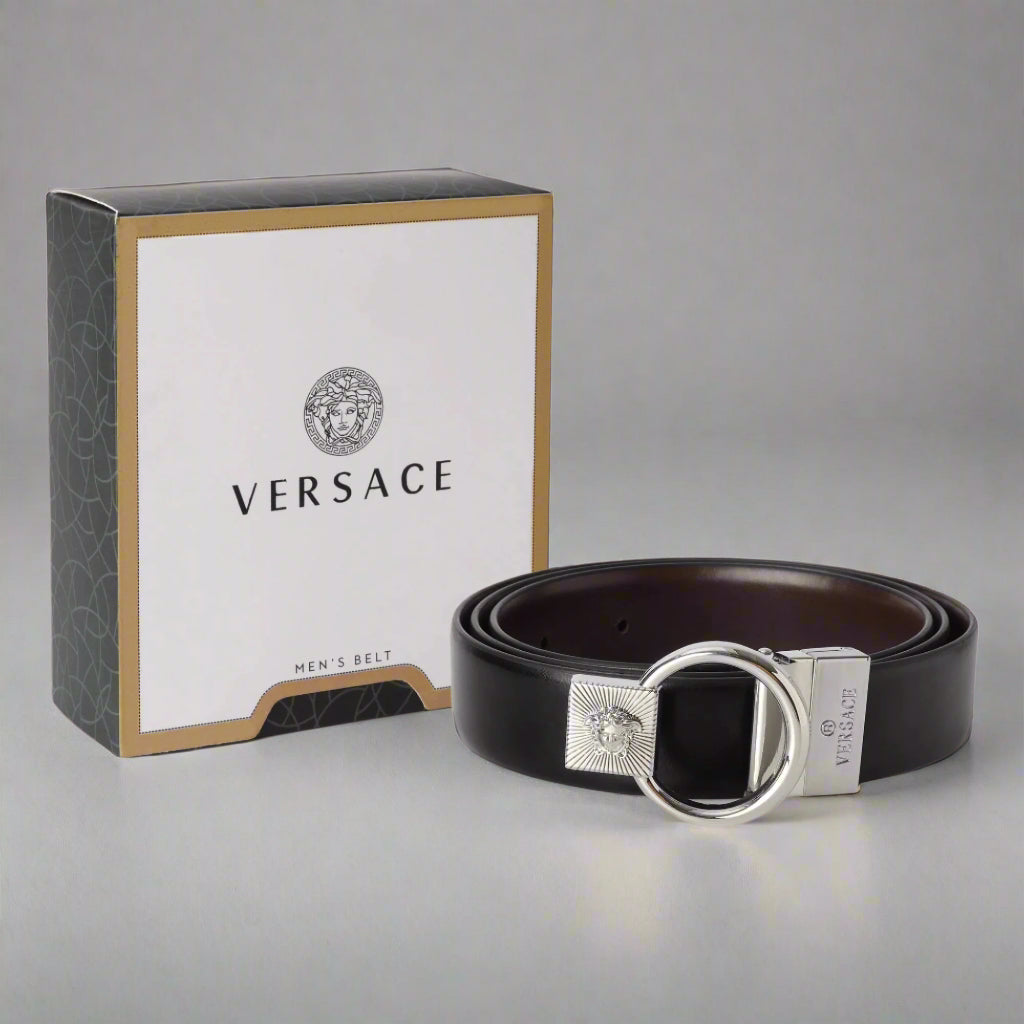 A black leather belt with a silver circular buckle featuring an engraved Medusa head, presented next to its packaging box with the Versace logo.